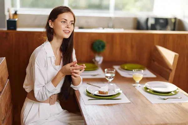 家でロマンチックな夕食を楽しむエレガントな女性 美しいブルネットの女性はスタイリッシュなセットのダイニングテーブルに座り 彼女は自家製の食事にふけるように静かに笑います テーブルはAで飾られています — ストック写真