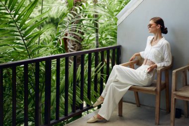 Gülümseyen Kadın Güneş Işığı ve Güzel Bitkilerle Rahatlatıcı Terasta Tropikal Tatilin keyfini çıkarıyor