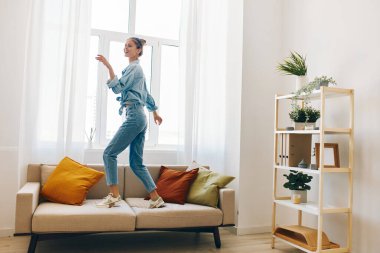 Evde Neşeli Zıplama: Neşeli Bir Kadın Dans Ediyor ve Rahatlatıcı Oturma Odasında Şarkı Söylüyor