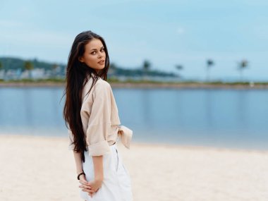 Stil Düşkünü Bayan Yaz Tatili: Esmer Güzel Genç Kadın Beyaz Kum Kumsalında Duruyor, Güzel Okyanus ve Günbatımı Gökyüzü ile Mutlu ve Rahat Görünüyor