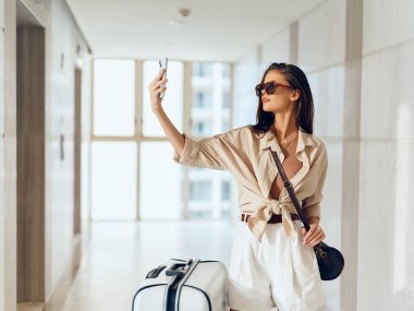 Neşeli Kadın Gezgin, Havalimanı Terminalinde Bekliyor, Akıllı Telefon ve Bavul Kullanılıyor