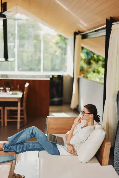 在舒适的客厅里 一个戴着眼镜 面带微笑的女人舒服地坐在一个现代客厅的沙发上 她是个成功的自由职业者 — 图库照片