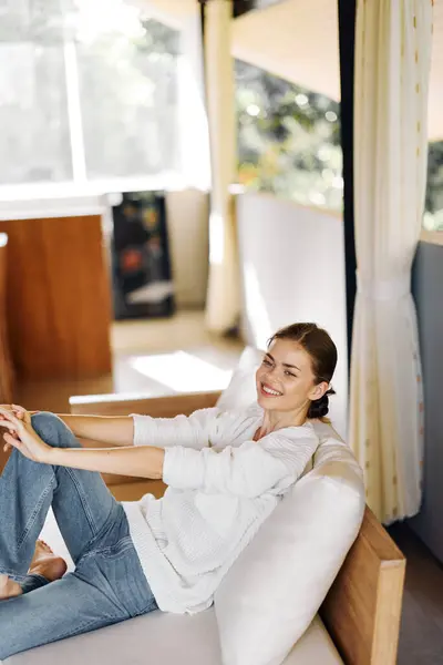 Happy Smiling Woman Sitting on Cozy Couch at Home, Enjoying Relaxing Moment in Stylish Knitwear Her Natural Beauty Shines Through as She Radiates Joy and Contentment The Warm and Inviting Living Room