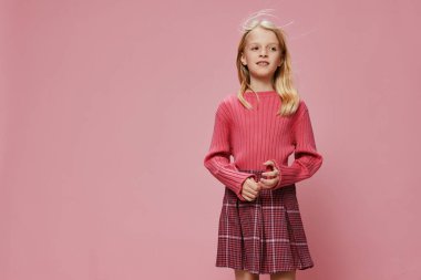 Şık pembe bir elbisesi ve büyük bir gülümsemesi olan mutlu bir kız öğrenci. Stüdyodaki kameraya heyecanlı ve şok olmuş bir şekilde bakıyor. Gençlik ifadesi ve düşünceli bakışları neşe ve merakını yansıtıyor.