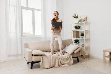 Oturma odasında dizüstü bilgisayarda çalışan gülümseyen kadın serbest yaşam tarzını benimsiyor.