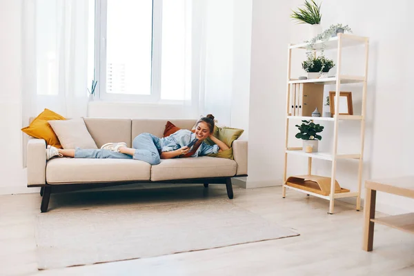 Smiling woman holding mobile phone, enjoying relaxation on cozy sofa at home: \