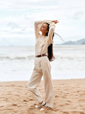 Yaz Saadeti: Çekici Kafkas Kadını Sahilde Şık Elbiseyle Tatilden Hoşlanıyor, Okyanus kıyısında Güneşli Mavi Gökyüzü Altında Mutlu ve Rahatlamış Hissediyor