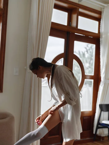 Young brunette woman at home in the morning. Sensual young woman with sexy body in shirt and white lingerie in modern apartment near window after waking up. weekend, vacation. High quality photo