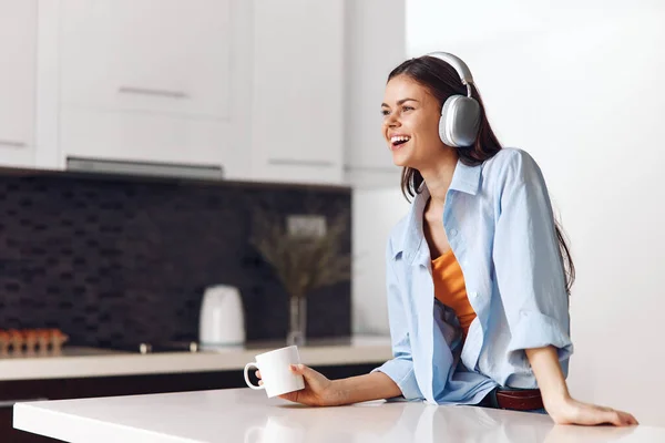 Woman enjoying a peaceful morning at home, listening to music with headphones and drinking coffee at kitchen counter