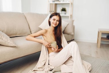 Sıcak bir fincan kahve: Gülümseyen bir kadın Evde Rahatlatıcı bir Sabahın tadını çıkarıyor, Battaniyeye sarılmış, Kanepeye Oturuyor