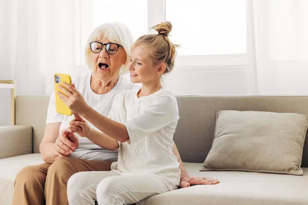 Video bonding call granddaughter child space phone white selfie t-shirt copy grandmother family two photography people sofa smiling education hugging togetherness indoors
