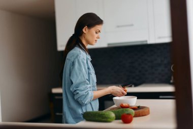 Taze ve sağlıklı: Genç, beyaz bir kadın, bir ev hanımı, Modern bir mutfakta vejetaryen salatası hazırlıyor.