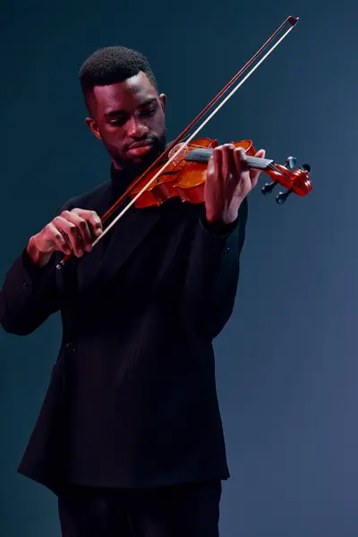 穿着黑色西装的优雅的非洲裔美国人在黑暗背景下演奏小提琴 — 图库照片