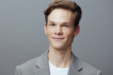 Sade arka planda gri ceketli, gülümseyen genç adam.