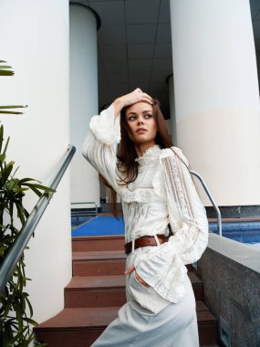 Modern şehir parkının arka planına karşı, şehvetli, genç ve modaya uygun bir havası olan açık havada yaz elbisesi içinde şık beyaz kadın pozu.