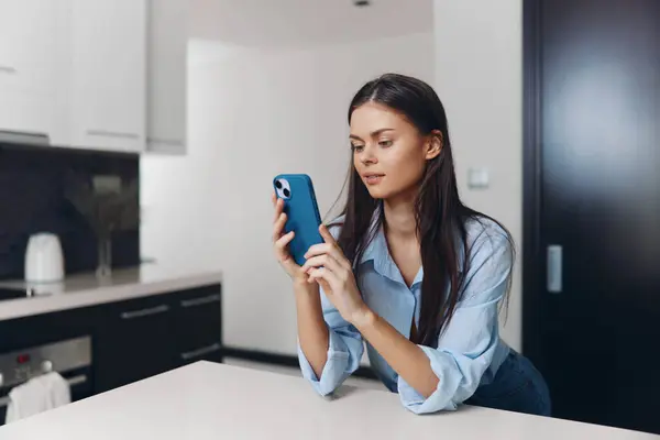 Mujer Joven Usando Teléfono Inteligente Mientras Está Sentado Mostrador Cocina —  Fotos de Stock