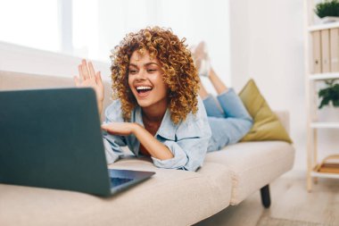 Oturma odasında dizüstü bilgisayarda çalışan gülümseyen kadın.