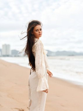 Deniz Güzeli: Şık Saçlı, Beyaz Kum Sahilinde Duran, Gün batımında Serene Okyanusu Manzarasının tadını çıkaran Güzel Genç Bir Kadın