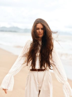 Şık Yaz Güzelliği: Beyaz Elbiseli Muhteşem Genç Bir Kadın, Güneşli Sahilde Rahatlıyor, Esmer Saçlı, Tropikal Okyanusun Özgürlüğünün ve Romantizminin Tadını Çıkartıyor