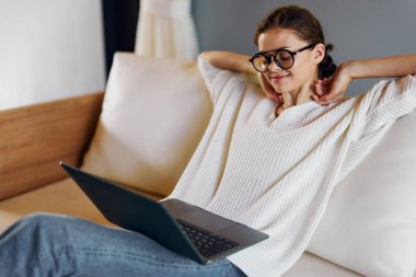 Konforlu İçişleri Ofisi 'nde dizüstü bilgisayarda çalışan mutlu kadın, Serbest Çalışan Yaşam Tarzı ve Başlangıç Başarı Tarifi' nin keyfini çıkaran bu modern iç mekan ortamında, güzel bir kadın rahat bir şekilde koltukta oturuyor.