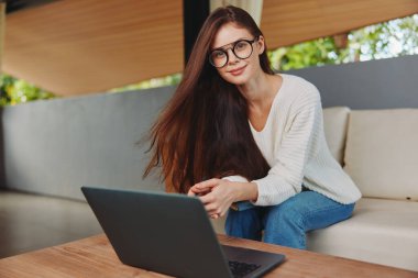 İçişleri Bakanlığı 'nda dizüstü bilgisayarla koltukta oturan Gülümseyen Kadın Çevrimiçi Eğitimin tadını çıkarıyor