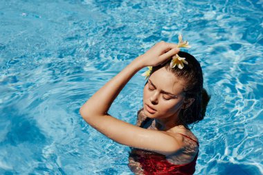 Yüzme havuzunda yüzen, kırmızı mayolu, güzel gülüşlü ve havuzda yüzen Bali çiçekli genç bir kadın. Tatilde rahatlama kavramı. Yüksek kalite fotoğraf