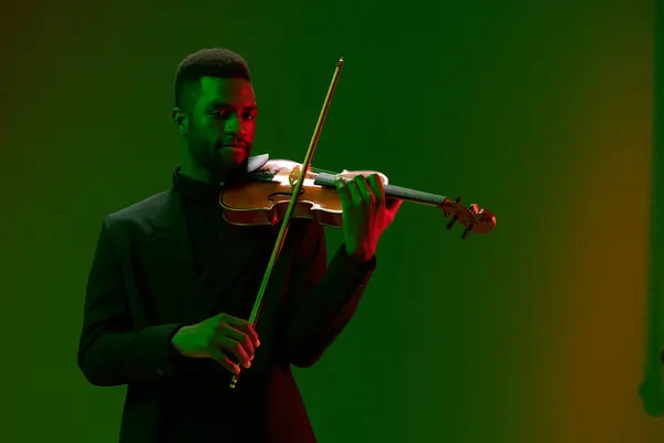 Elegant man in formal attire playing violin in front of vibrant green and red background