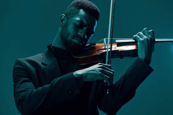 Elegant man in black suit playing the violin with passion on a vibrant blue background