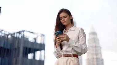 Sokakta elinde telefonla gezen bir kadın öğleden sonra gökdelenlere bakan bir arka planda yaşayan bir iş kadını ve serbest çalışan bir turist. Yüksek kalite 4k görüntü