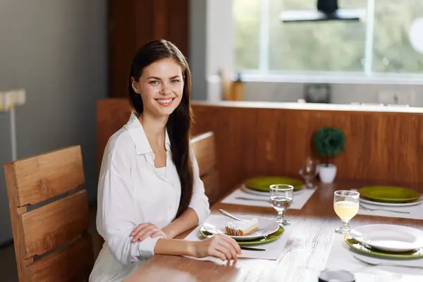 A Romantic Dinner Date at Home Enjoying a delicious homemade meal together, a beautiful and smiling brunette woman sits at a trendy dining table, adorned with elegant tableware and a plate filled with