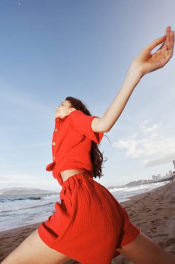 Neşeli Gülümseyen Kadın Deniz kenarında Güneşli bir plajda Kırmızı Yaz Kıyafetleriyle Dans Ediyor