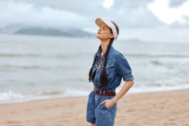 Güzel bayan plajda rahatlatıcı bir yaz tatilinin tadını çıkarıyor, güneşli bir gökyüzü altında ışıldayan mavi okyanus dalgalarına bakıyor.