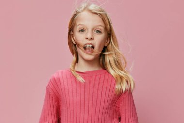 Şık pembe elbiseli mutlu bir kız öğrenci ve büyük bir gülümseme, fotoğraf stüdyosunda kendine güvenerek poz veriyor. İfade dolu yüzü ve neşeli ifadesi çocukluğun saf neşesini yansıtıyor.