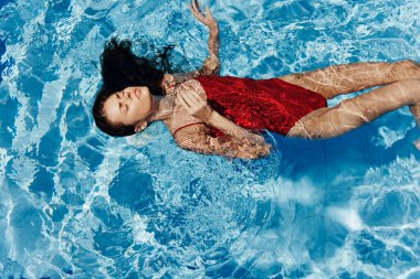 Havuzda yüzen kırmızı mayo giymiş, suda uzanan ve havuzda yüzen güzel bir gülümsemesi olan genç bir kadın. Tatilde dinlenme kavramı. Yüksek kalite fotoğraf