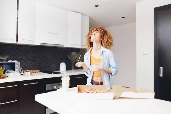 Woman standing in kitchen with pizza and box of doughnuts in front of her, preparing delicious homemade treats