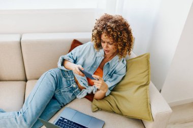 Modern Yaşam Tarzı: Laptop 'ta kulaklıkla gülümseyen kadın, rahat oturma odasında koltukta oturan kadın