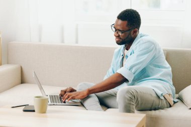 Modern Oturma Odası 'nda dizüstü bilgisayarda çalışan gülümseyen Afrikalı Amerikalı Adam, Çevrimiçi Alışveriş için çağrı yapıyor,