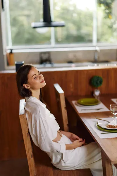 Romantic Dinner at Home Woman Smiling and Enjoying a Delicious Meal at a Stylish Dining Table The beautiful brunette woman is sitting in a trendy dining room, celebrating a romantic date night She