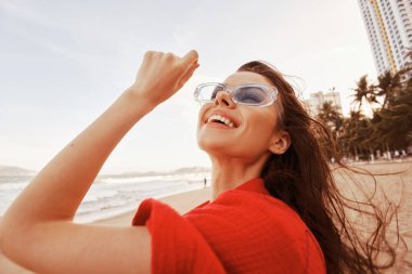 Sahilde neşeli bir kadın, açık ağızla gülümseyen, özgürlüğün ve renkli günbatımının tadını çıkaran