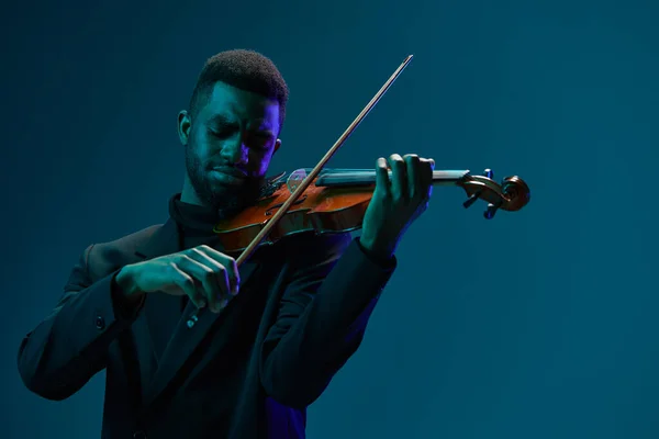 活気に満ちたブルーのバックグラウンドでヴァイオリンを演奏する黒いスーツのエレガントなミュージシャン — ストック写真