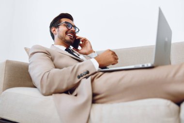 Erkek işadamı kanepede dizüstü bilgisayarla yatıyor ve telefonla konuşuyor, iş ve veri analizlerinde online video teknolojisi, iyi anlaşma, yaşam tarzı yöneticisi. Yüksek kalite fotoğraf