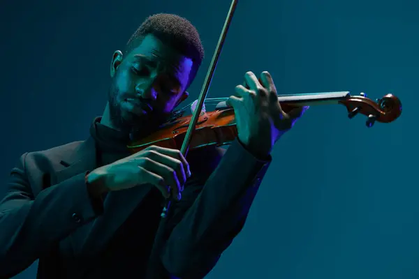 穿着黑色西服的优雅的男性音乐家 在充满活力的蓝色背景下演奏小提琴 — 图库照片