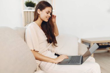 Oturma odasında dizüstü bilgisayar kullanan gülümseyen kadın, evden serbest çalışıyor.