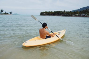 Kayak Macerası: Mutlu Asyalı Adam Tropikal Sahilde Su Sporunun keyfini çıkarıyor