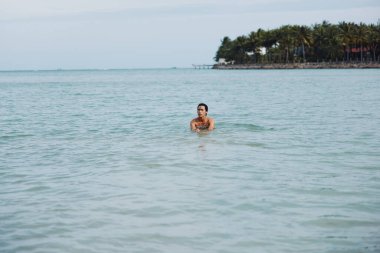 Neşeli Asyalı Adam Tropikal Okyanus sularında yüzüyor Mavi Gök 'ün altında gülümsüyor