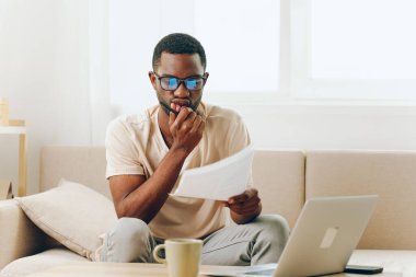 Modern İçişleri Bakanlığı 'nda dizüstü bilgisayarda çalışan gülümseyen Afrikalı Amerikalı Serbest Çalışan genç siyahi adam rahat bir koltukta oturuyor, bilgisayarında mutlu bir ifadeyle daktilo yazıyor.