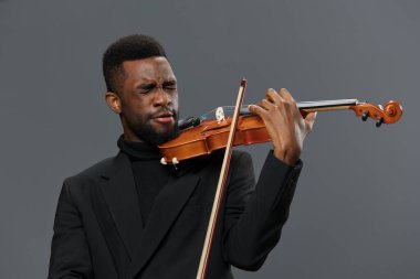 Siyah takım elbiseli Afrikalı bir adam zarif müzik performansı konseptiyle gri arka planda keman çalıyor.