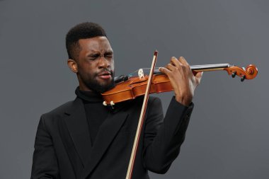 African American man in black suit playing violin on gray background in elegant musical performance concept clipart