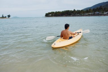Serene Tropikal Kaçış: Palmiye püsküllü bir plajda kayak yapan mutlu bir Asyalı adam