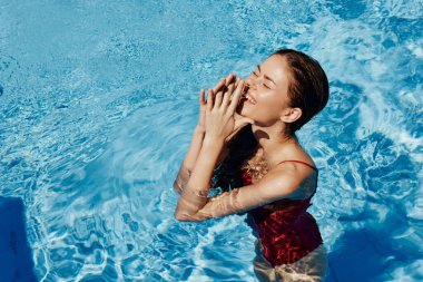 Kırmızı mayo içinde yüzen, uzun saçlı, güneş kremli cilt koruması olan, tatilde rahatlama konsepti olan mutlu bir kadın. Yüksek kalite fotoğraf